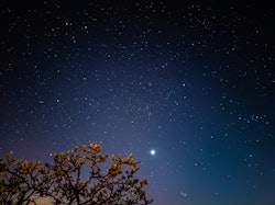 An image of the night sky with the planet Venus noticeably brighter than other stars. What planet ru...