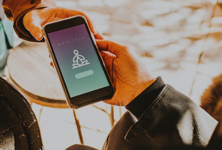 A hand holds a smart phone that displays a generic meditation app as another hand takes the phone.