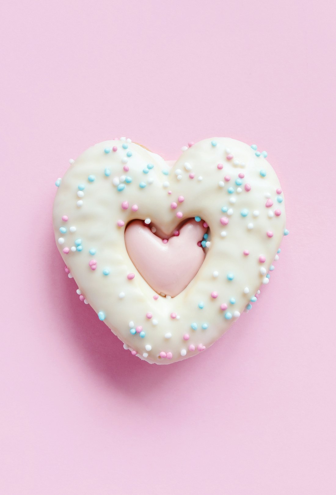 Flat lay of heart shaped gingerbread cookie with sprinkles and icing on pink background. Top view of...