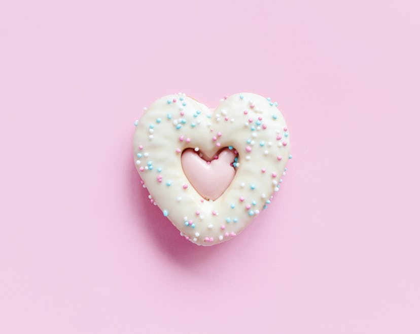 Flat lay of heart shaped gingerbread cookie with sprinkles and icing on pink background. Top view of...