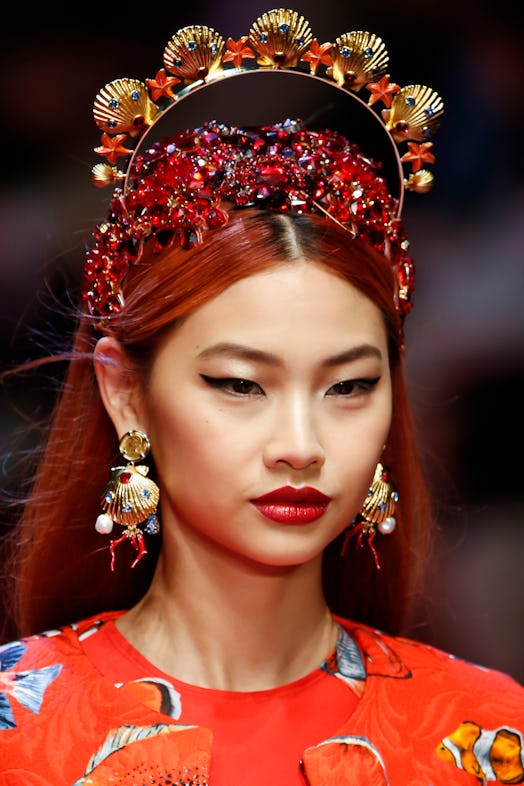A model walks the runway wearing large earrings and a jeweled headpiece at Dolce and Gabbana’s show …