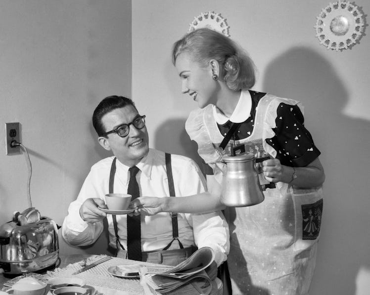 1950s COUPLE AT BREAKFAST TABLE MAN READING NEWSPAPER SMILING AT WIFE HOLDING COFFEE CUP AND PERCOLA...