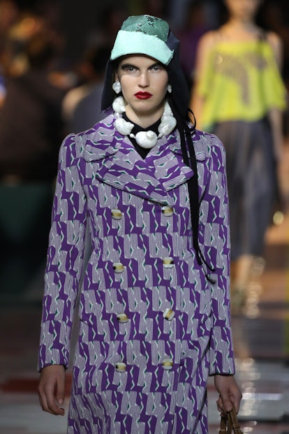 A model walks the runway at the Prada show in shell accessories and a patterned coat.