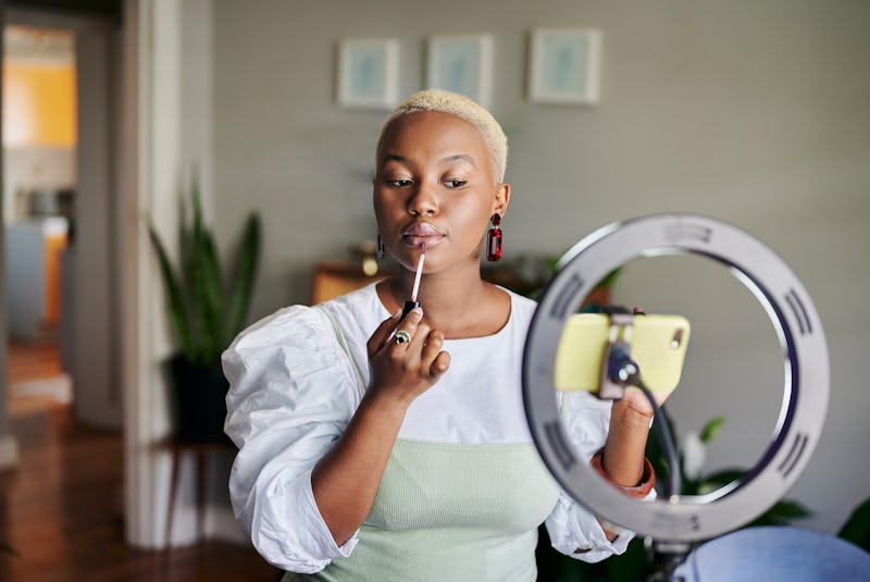 A  beauty blogger filming herself applying a Dior Lip Glow dupe lip gloss in front of a ring light. 