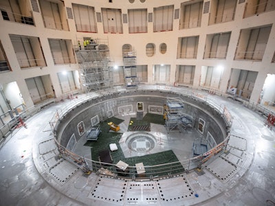 Technicians work on the bioshield inside the Tokamak Building with the base of the cryostat at its b...