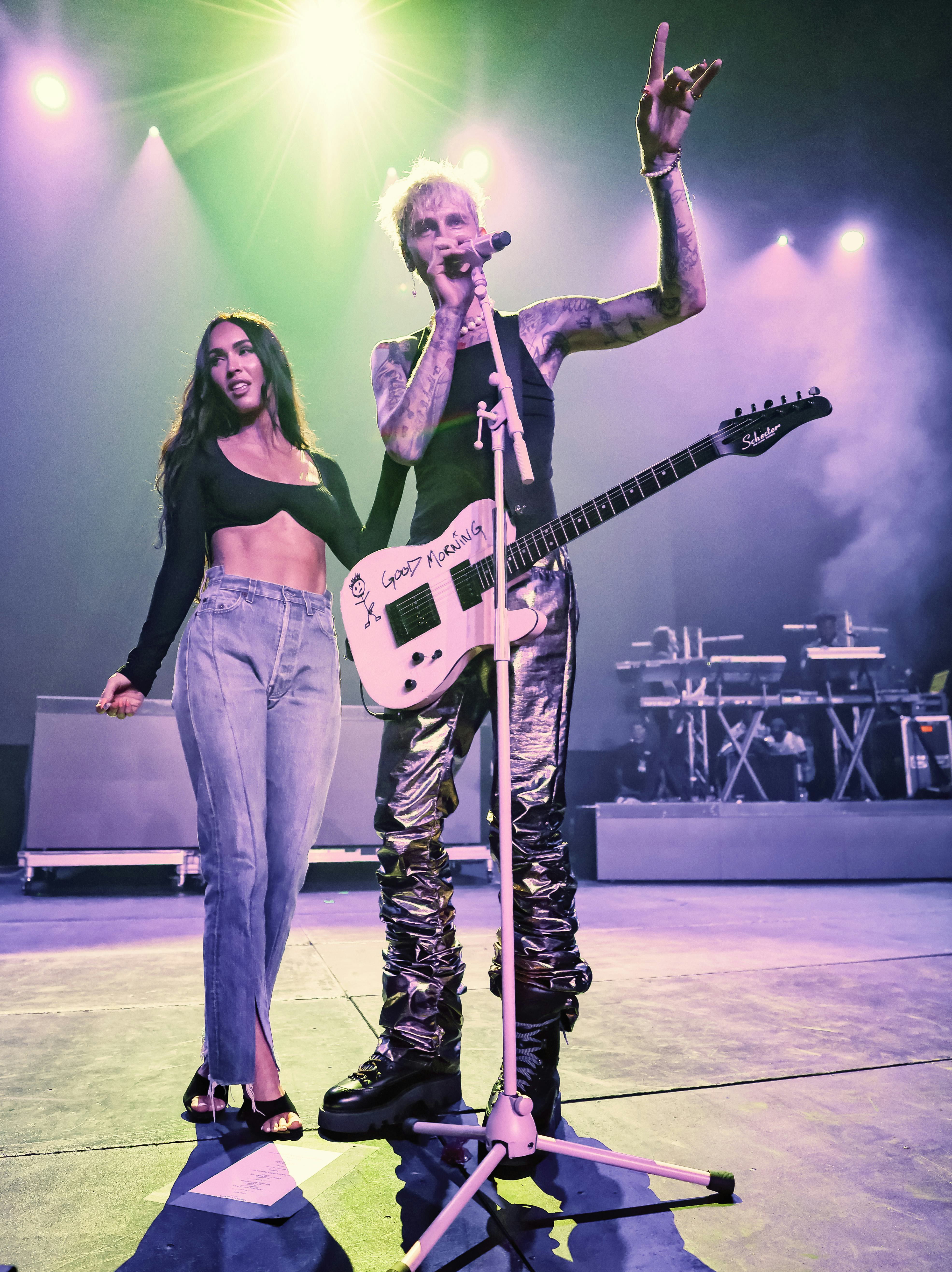 Megan Fox in a crop top and jeans and Machine Gun Kelly in a black tank and shiny pants.