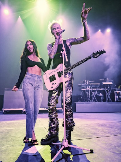 Megan Fox in a crop top and jeans and Machine Gun Kelly in a black tank and shiny pants. 