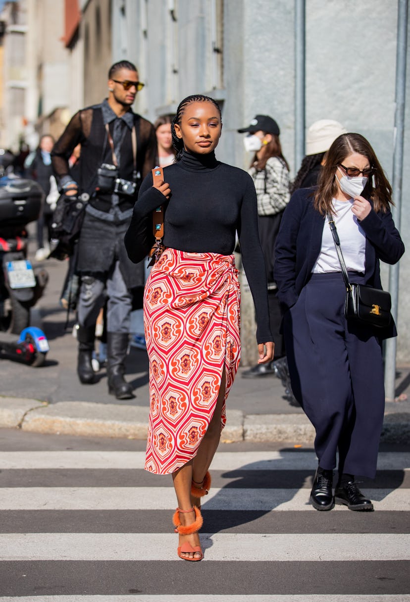 MILAN, ITALY - FEBRUARY 25: A guest is seen  wearing wrapped red skirt with print, black turtleneck,...