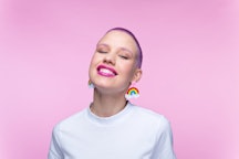 Cheerful young woman wearing white t-shirt and funny rainbow earrings smiling at camera. Studio port...