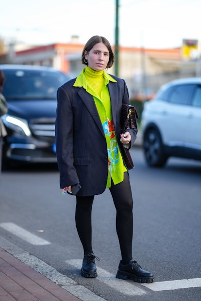 MILAN, ITALY - FEBRUARY 25: A guest wears gold earrings, a neon yellow ribbed turtleneck pullover, a...