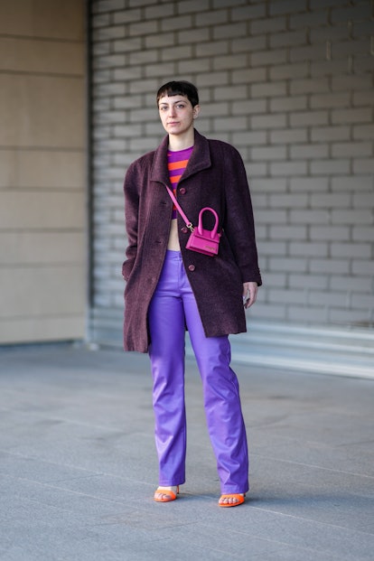 MILAN, ITALY - FEBRUARY 26: A guest wears rhinestones earrings, a purple and orange striped print pa...