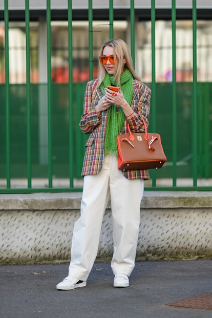MILAN, ITALY - FEBRUARY 25: A guest wears neon orange sunglasses, a green embossed print pattern sca...