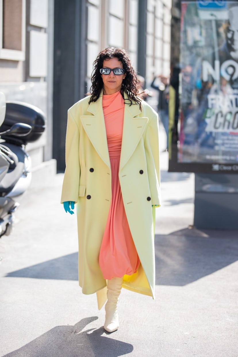 MILAN, ITALY - FEBRUARY 25: A guest is seen wearing yellow coat, salmon colored skirt, green gloves,...