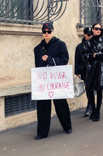 MILAN, ITALY - FEBRUARY 24: A guest wears all black and carries a "No War In Ukraine" white shopping...