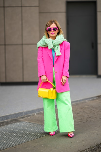 MILAN, ITALY - FEBRUARY 24: A guest wears neon pink sunglasses, a pale green wool pullover, a neon b...