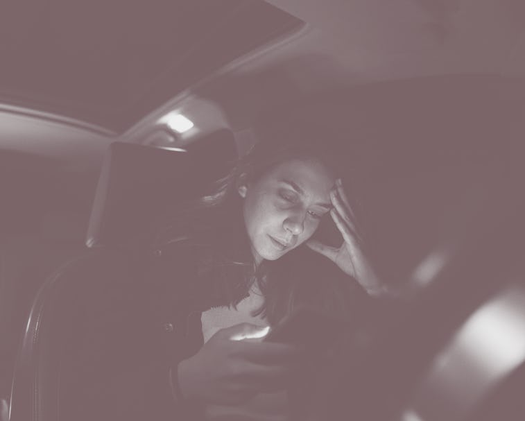Worried and abused Caucasian teenage girl, sitting in the car and using mobile phone