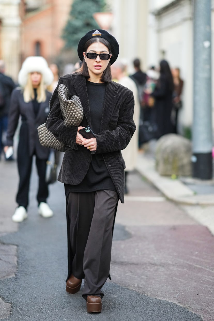 MILAN, ITALY - FEBRUARY 23: A guest wears a black felt beret with an embroidered logo, black sunglas...