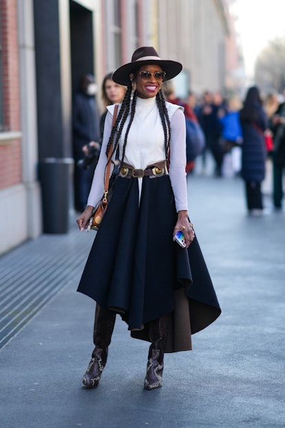 MILAN, ITALY - FEBRUARY 23: A guest wears a brown suede with white latte ribbon hat, sunglasses, gol...