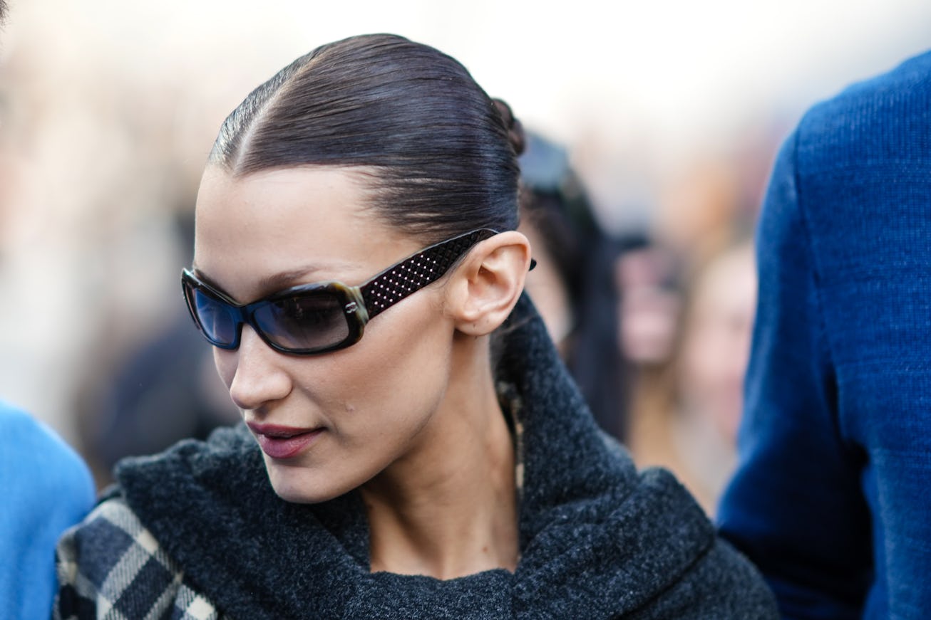 MILAN, ITALY - FEBRUARY 24: Bella Hadid wears black sunglasses, a black large scarf, a black and whi...