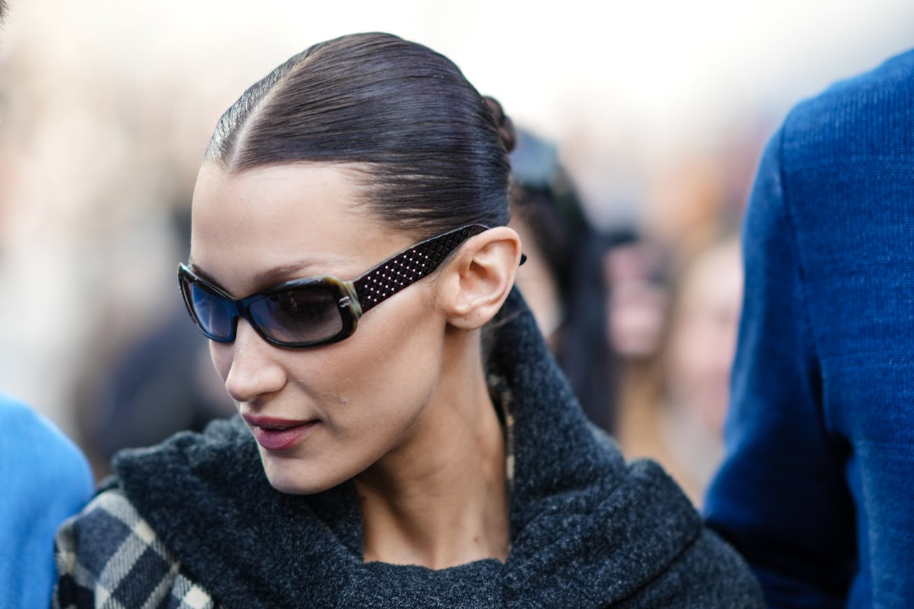MILAN, ITALY - FEBRUARY 24: Bella Hadid wears black sunglasses, a black large scarf, a black and whi...