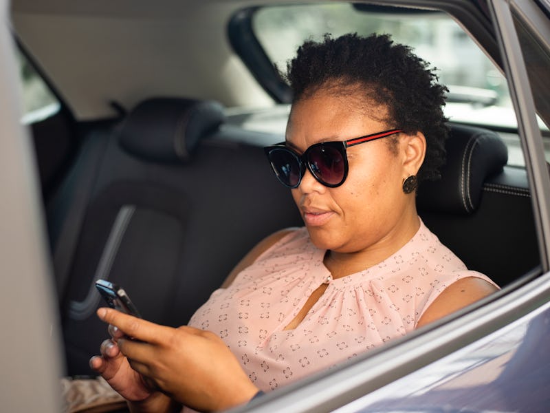 Stylish African woman checking an app on her smart phone while sitting in the back seat of a taxi