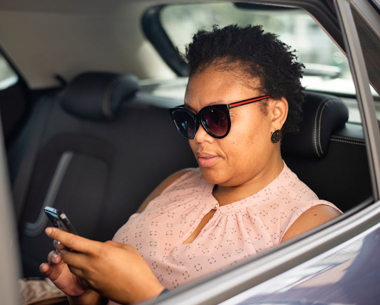 Stylish African woman checking an app on her smart phone while sitting in the back seat of a taxi