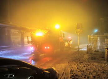 12 December 2021, Hessen, Schmitten: A snowplough spreads road salt on the snow-covered summit of th...