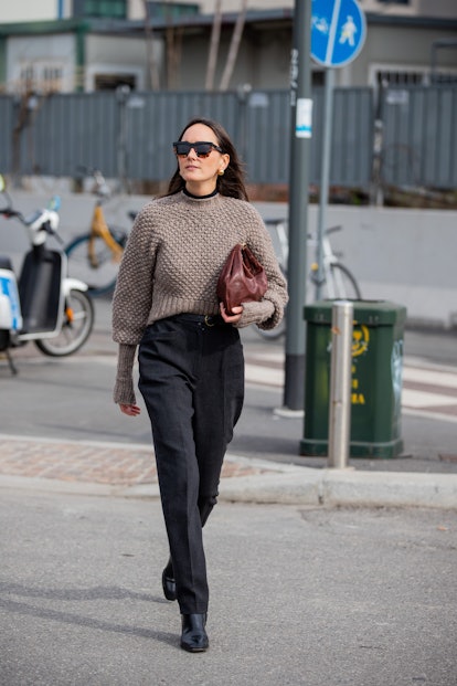 MILAN, ITALY - FEBRUARY 24: A guest is seen wearing brown bag, dark denim jeans, jumper outside Sunn...