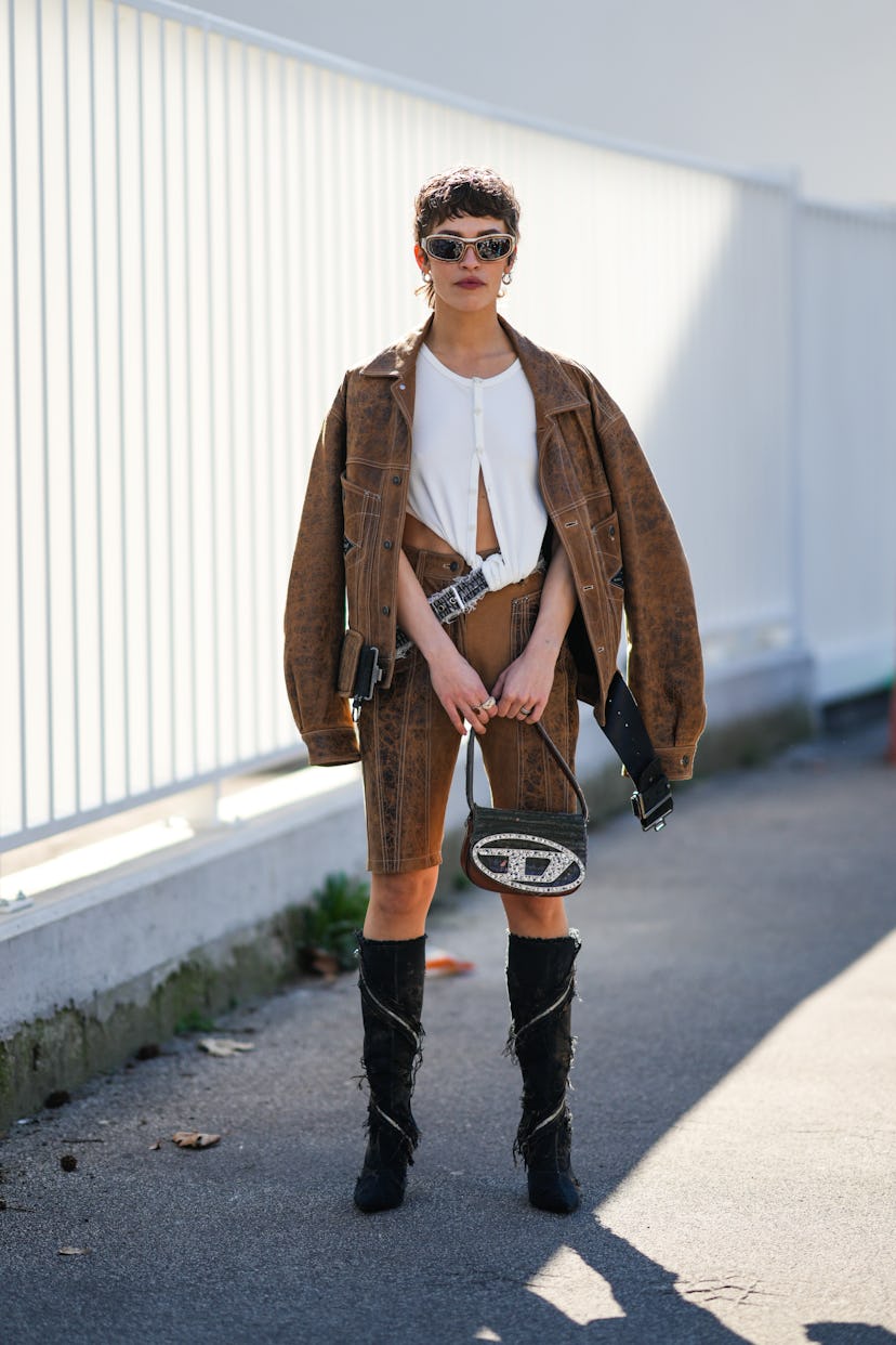 MILAN, ITALY - FEBRUARY 23: A guest wears beige and brown sunglasses, silver earrings, a white ribbe...