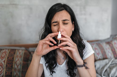 Young woman sick at home spraying nasal spray.