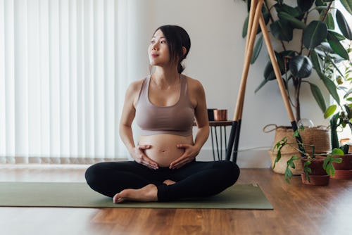 Beautiful young Asian pregnant woman resting after doing pregnancy yoga at home. Healthy and active ...
