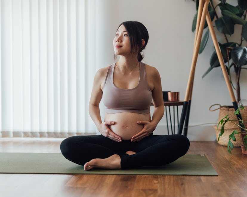 Beautiful young Asian pregnant woman resting after doing pregnancy yoga at home. Healthy and active ...