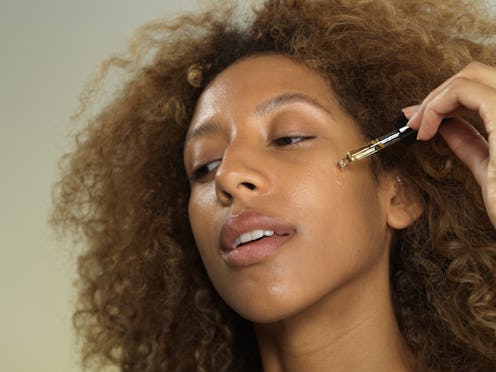 Woman of color dripping oil from pipette onto her face.