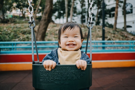 Happy baby girl smiling joyfully playing on swing in playground