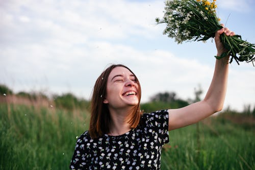 Young woman holding bunch of summer wild flowers in meadow outdoors in sunny day. Here's how the Mar...