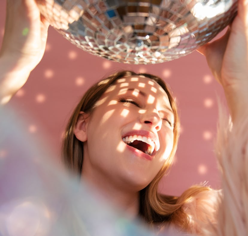Young woman laughing under a disco ball, knowing the week of March 21, 2022 will be the best for her...