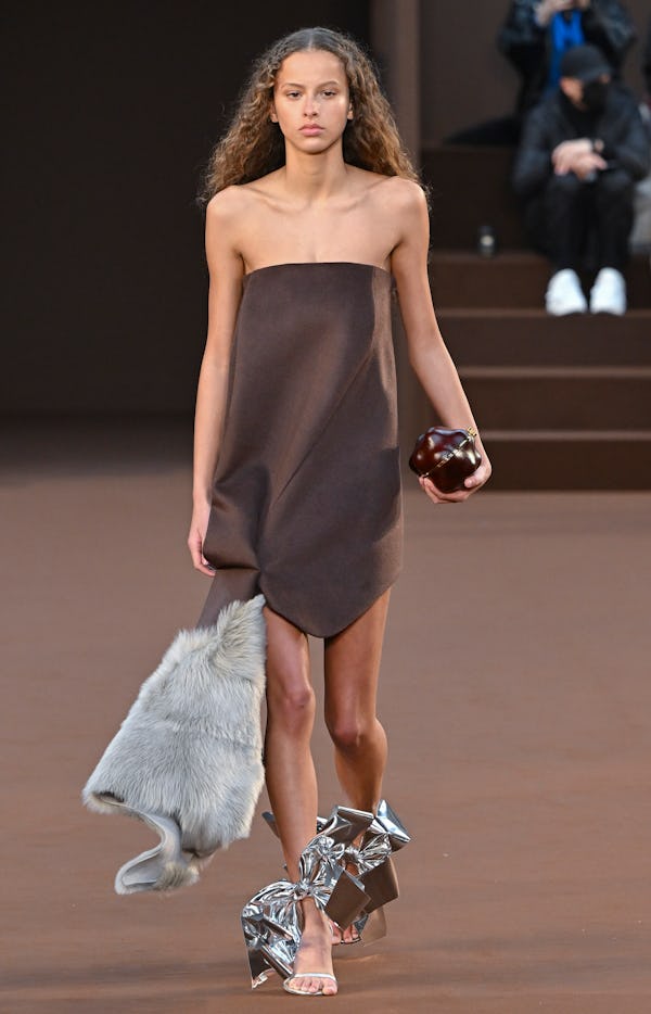 a model wearing a brown strapless mini dress with fur and silver bow strappy sandals on the Loewe ru...