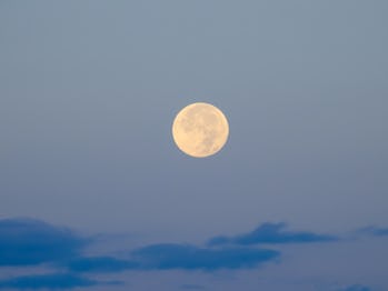 Full moon on a brightening dawn sky, above dark blue clouds