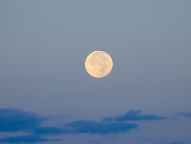 Full moon on a brightening dawn sky, above dark blue clouds