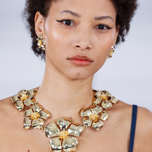 a model wearing gold flower earrings and a flower necklace on the Carolina Herrera runway