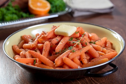 Serving dish of honey glazed baby carrots seasoned with salt, pepper, thyme and butter. It sits on a...