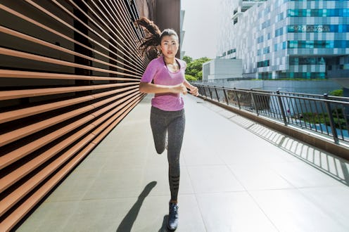 A young asian woman is jogging through the city of Singapore in the early morning. She passes a sect...