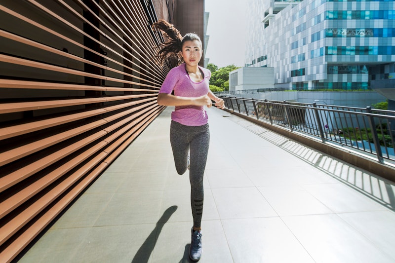 A young asian woman is jogging through the city of Singapore in the early morning. She passes a sect...