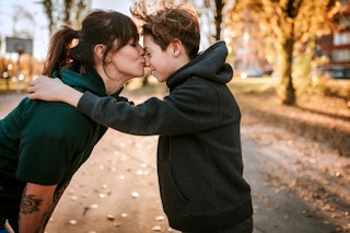 Young woman kissing and embracing her son outdoor, standing face to face on sunny day