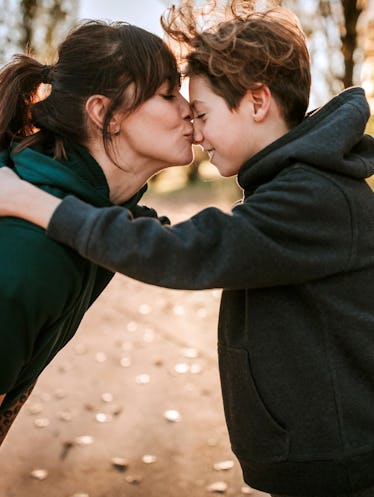 Young woman kissing and embracing her son outdoor, standing face to face on sunny day