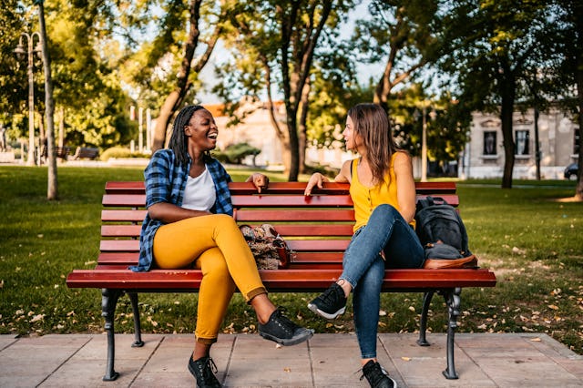 Two female multi-ethnic friends talking on a park bench.