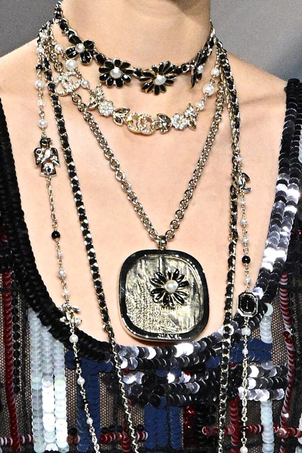 a model wearing layered necklace including a flower choker and large floral pendant on the Chanel ru...