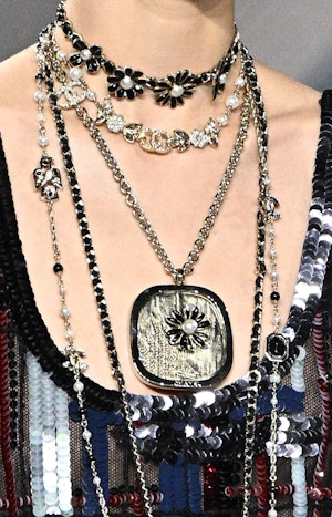 a model wearing layered necklace including a flower choker and large floral pendant on the Chanel ru...