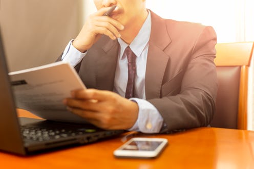 Businessman reading paperwork form with laptop on wooden desk