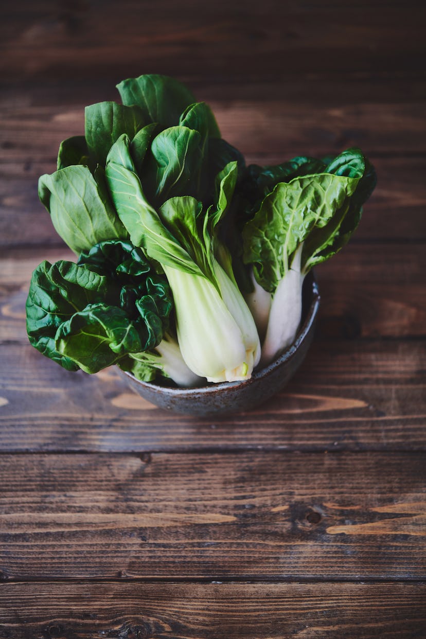 Ceramic bowl filled with bok choy on a rustic wood table. Space for copy